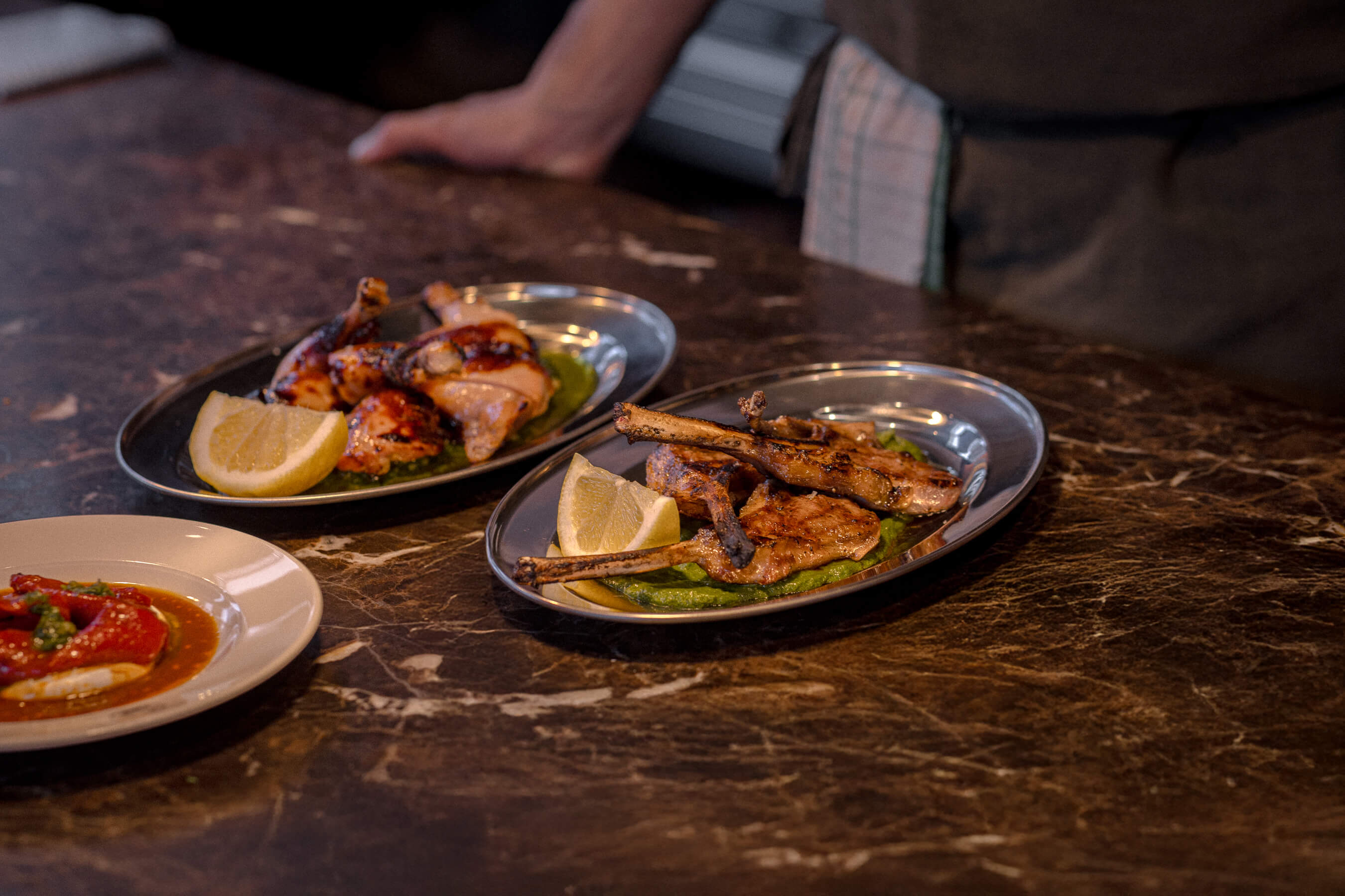 Chef’s station at Le Foote featuring plated lamb and chicken dishes, with dockets, lemon wedges and pass cloth in view