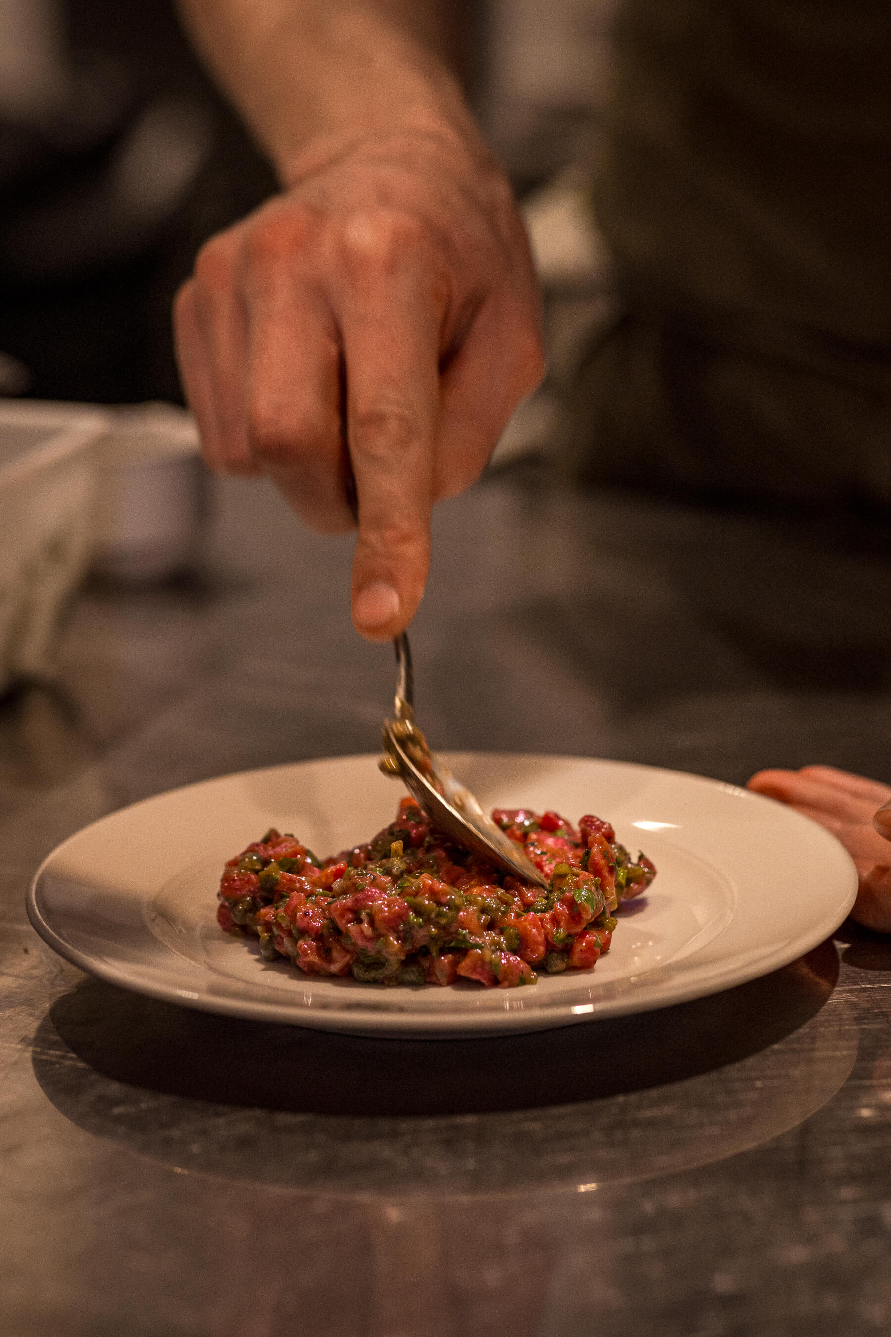 Close-up of chef’s hand shaping steak tartare on a white plate at Le Foote, styled with care for plating consistency