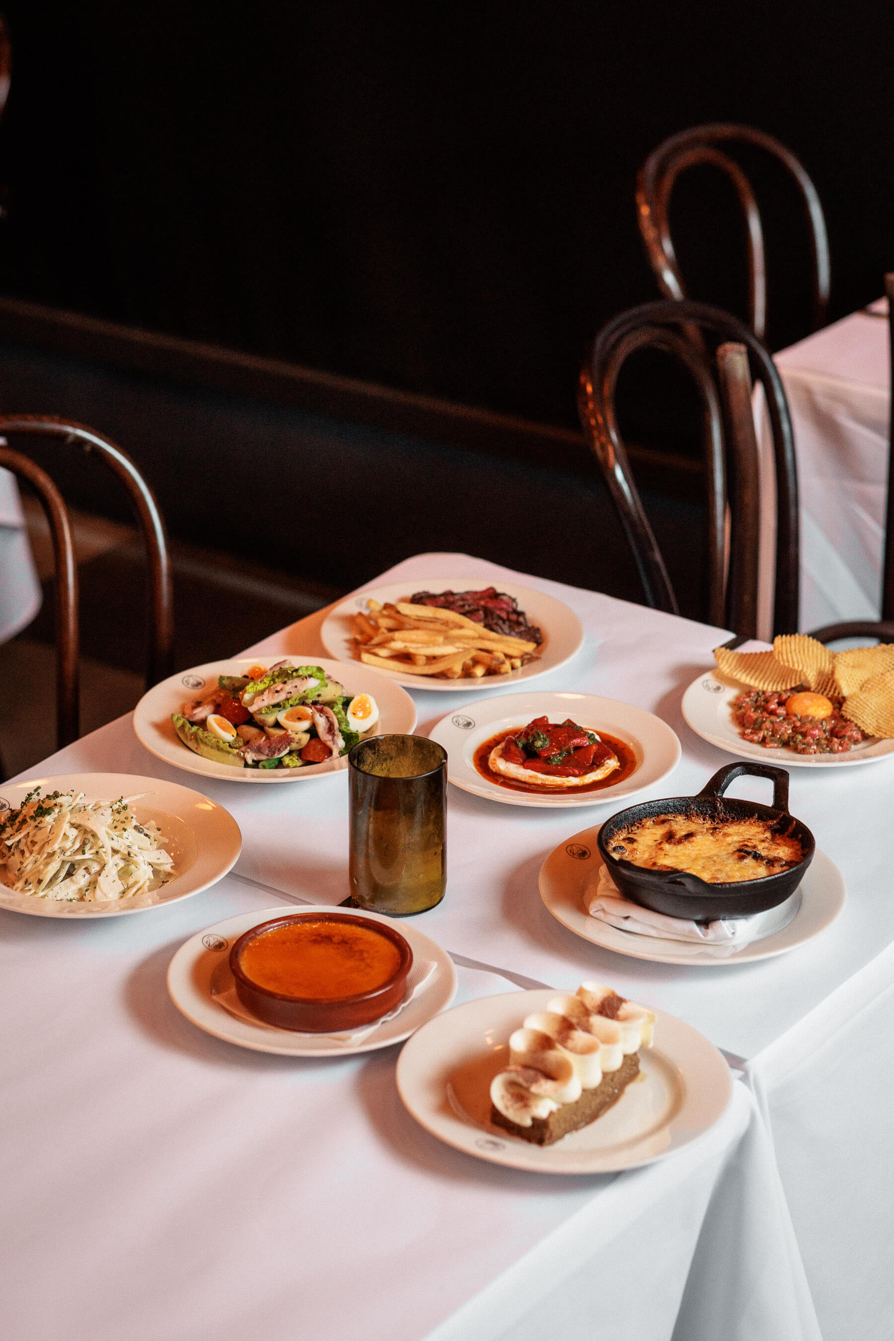 Assorted dishes on white tablecloth at Le Foote Sydney including steak frites, salad, crème brûlée, and gratin