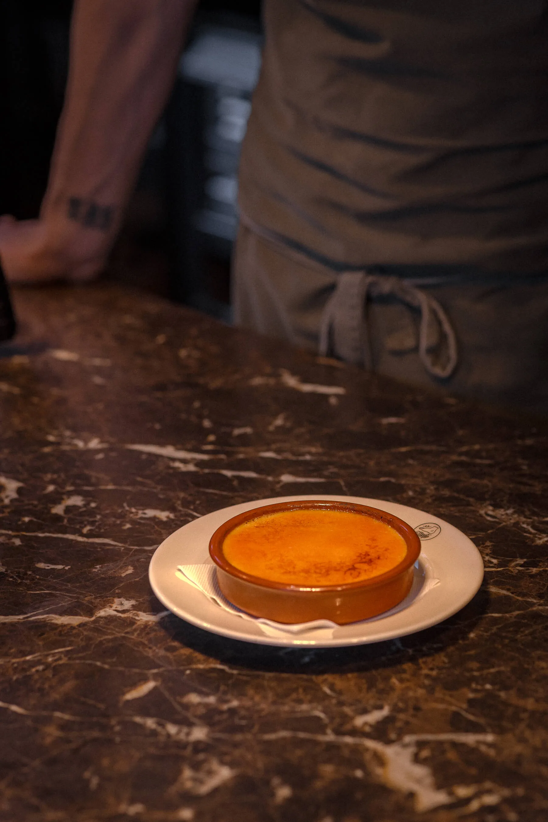 Classic crème brûlée served in a ceramic dish on marble countertop at Le Foote, Sydney, with chef in the background | EDG Studios