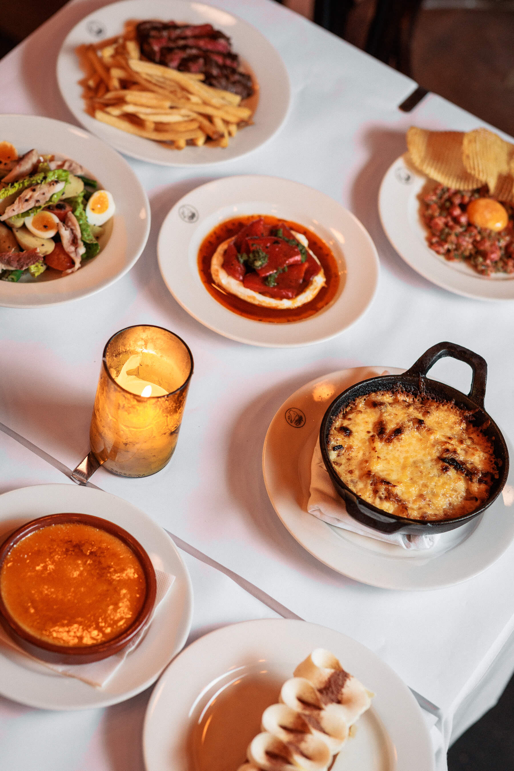 Warmly lit dinner setup at Le Foote with steak, fries, whipped cheese, carrot cake, and golden candle glow