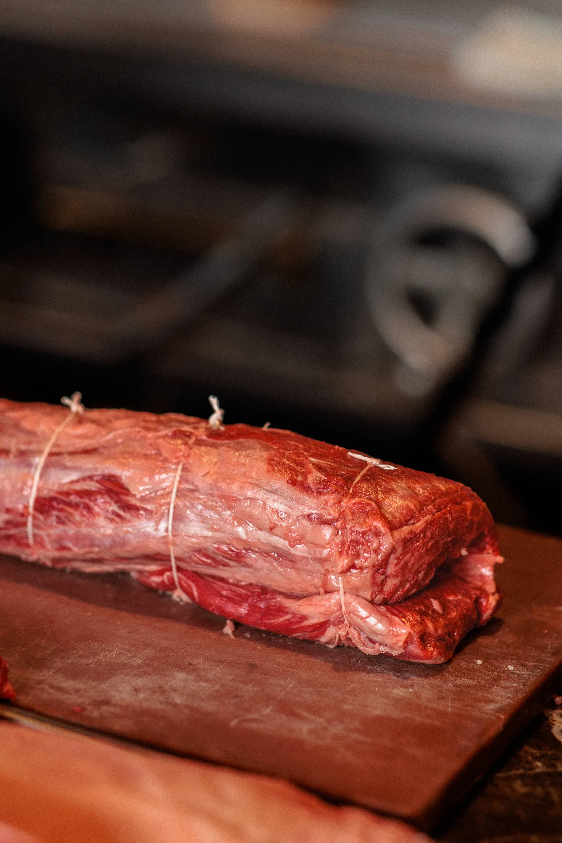 A tightly tied beef cut resting on a wooden board in a softly lit kitchen, ready for cooking at Le Foote | EDG Studios