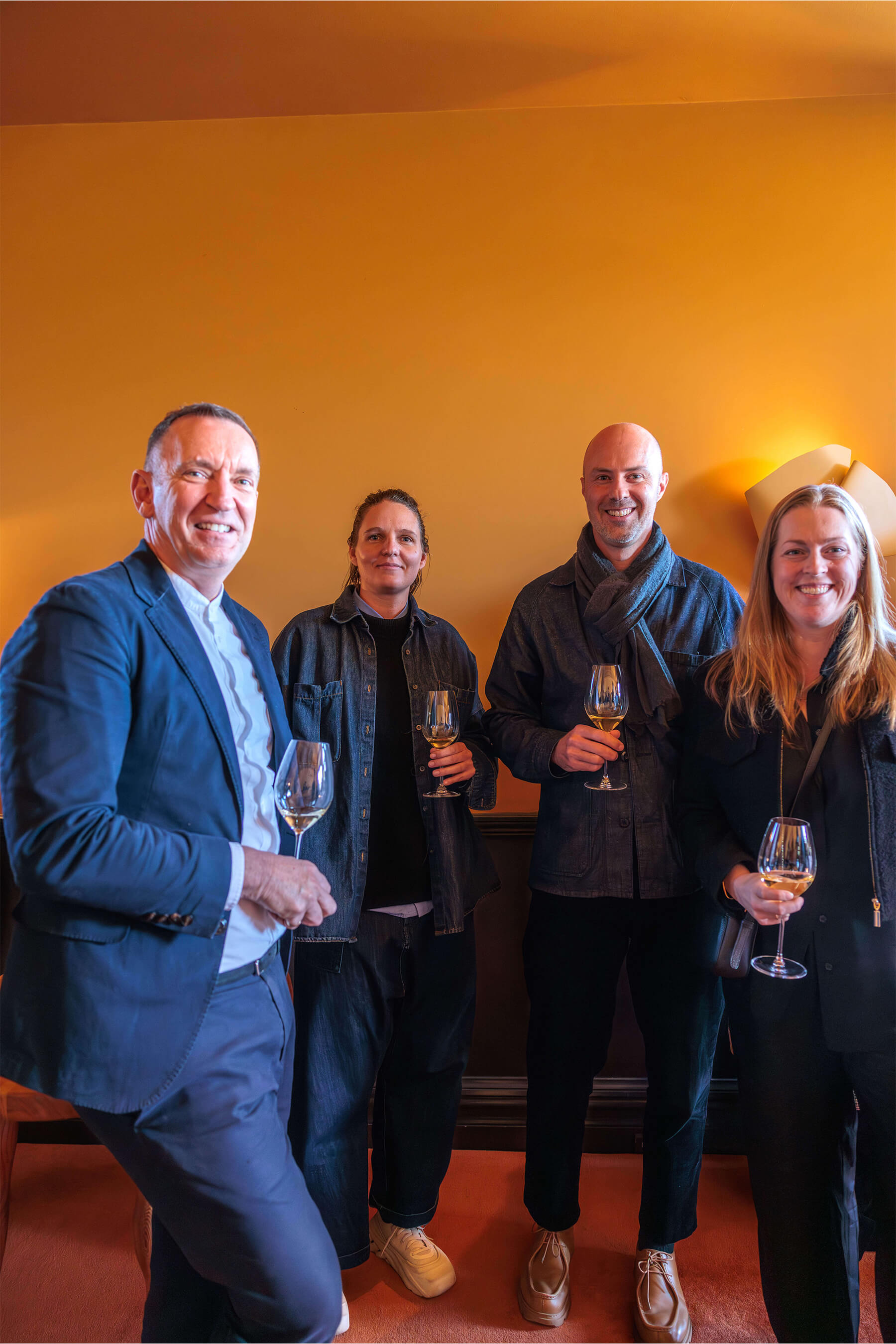 A group of four event guests holding glasses of wine and smiling at the camera, dressed in dark and denim tones, gathered at the Royal Oak Floors launch.