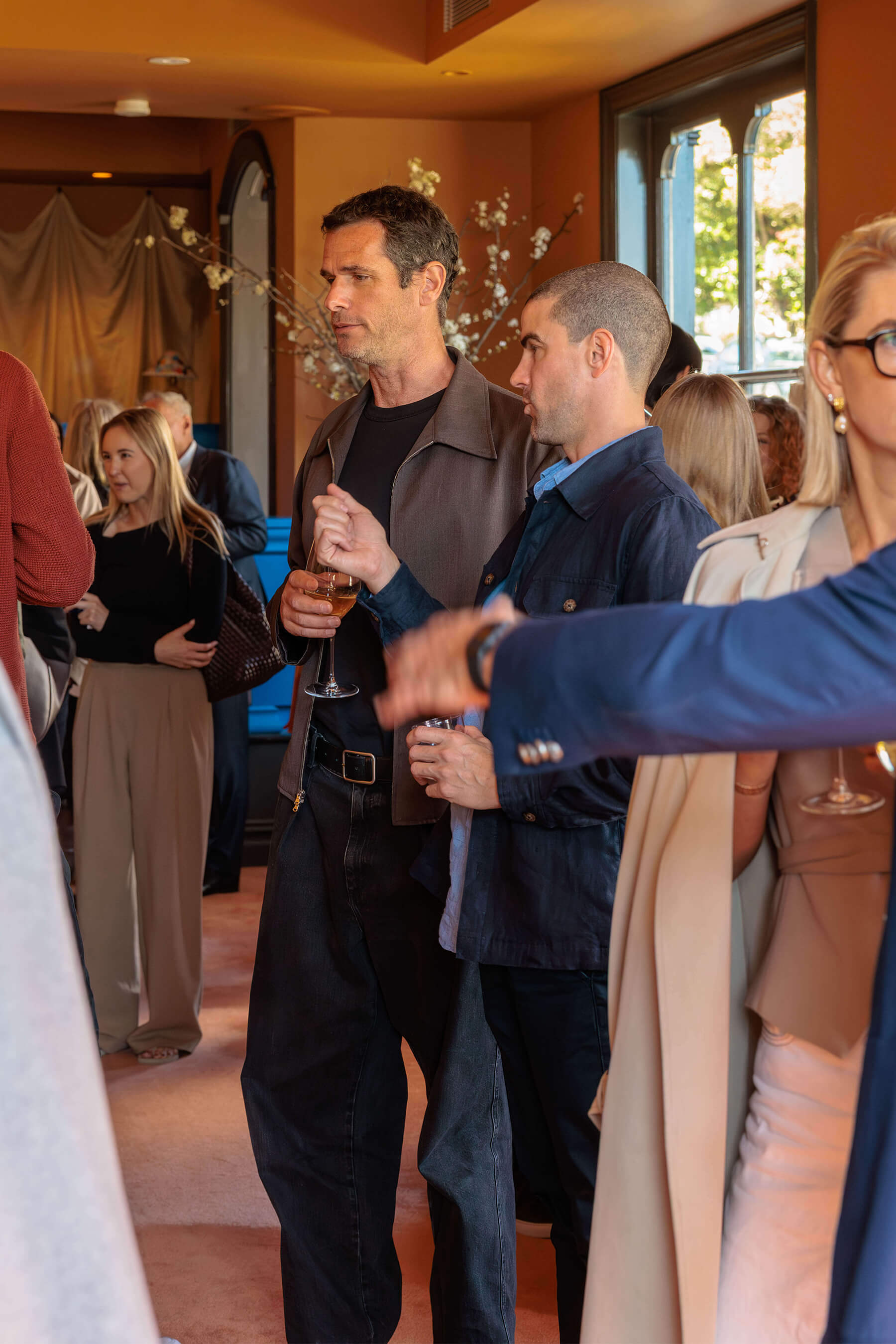 Two male guests talking over drinks at the Royal Oak Floors launch, surrounded by groups of attendees in Ursula’s dining room.