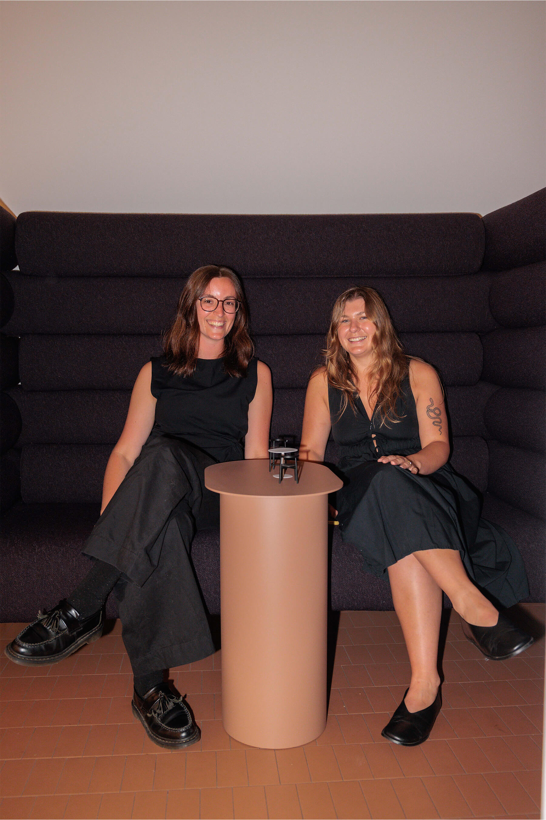 Two women seated on a sculptural dark purple lounge at the DesignByThem event, dressed in black and sharing a relaxed moment before the Q&A.