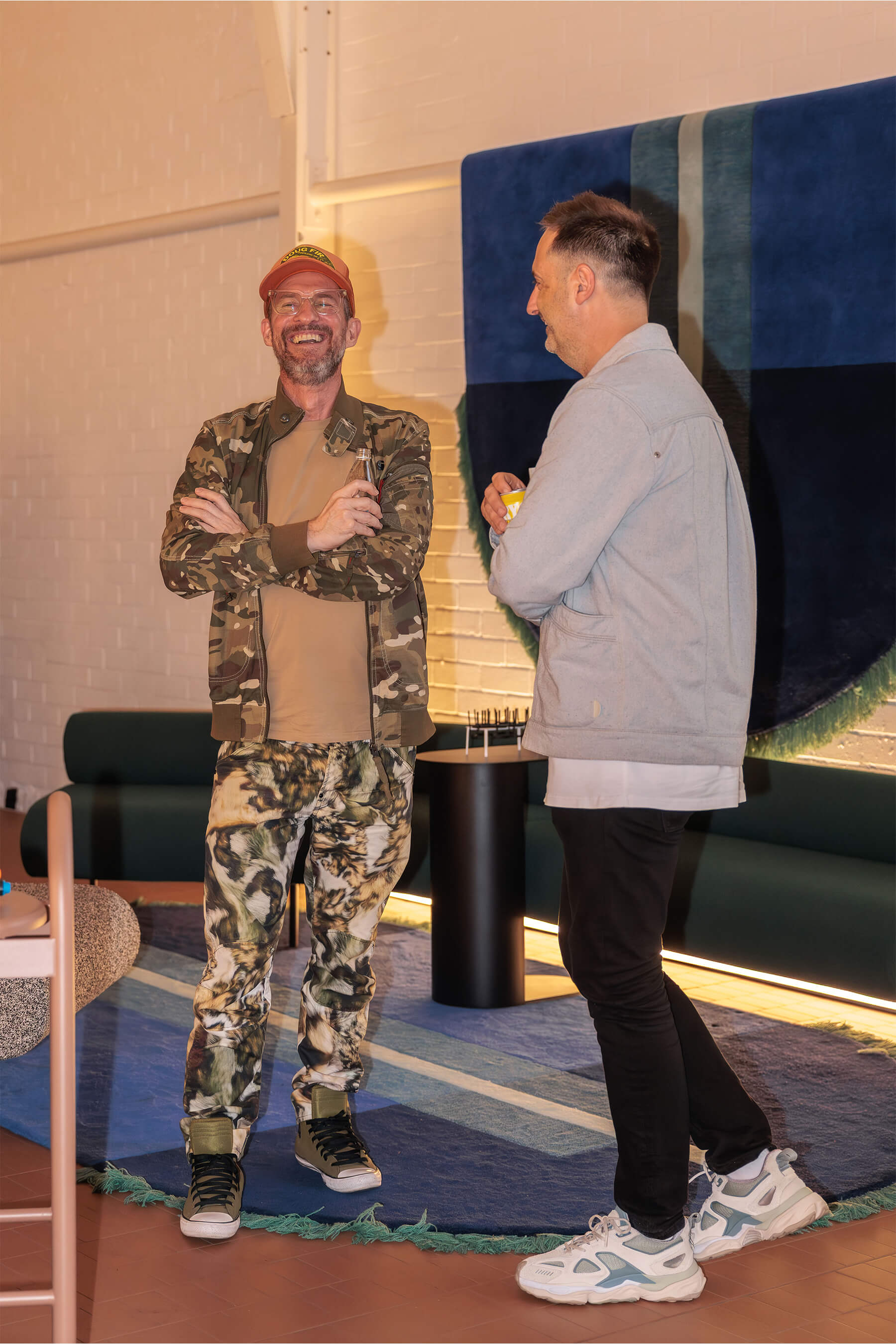 An attendee in printed camo attire shares a laugh with another guest during the DesignByThem “I’ll Be Happy When” event surrounded by styled interiors.