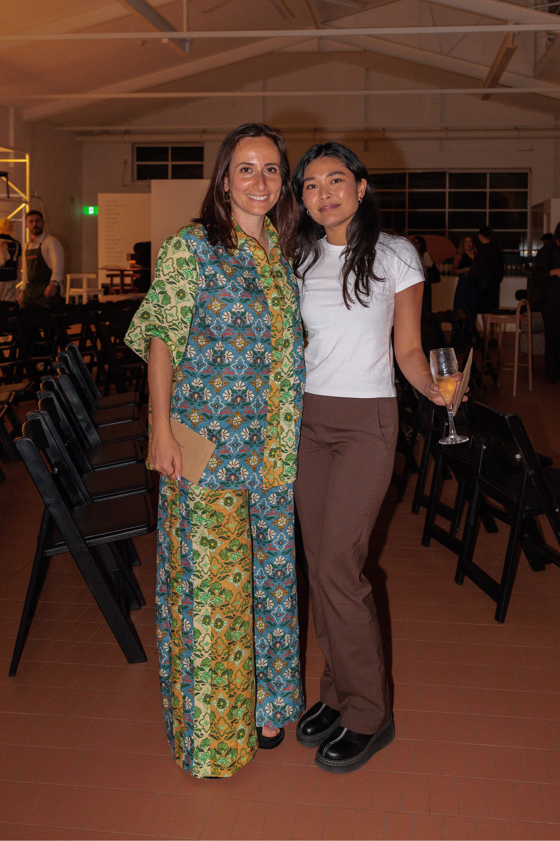 Two attendees standing arm in arm in the event space following the DesignByThem panel discussion.