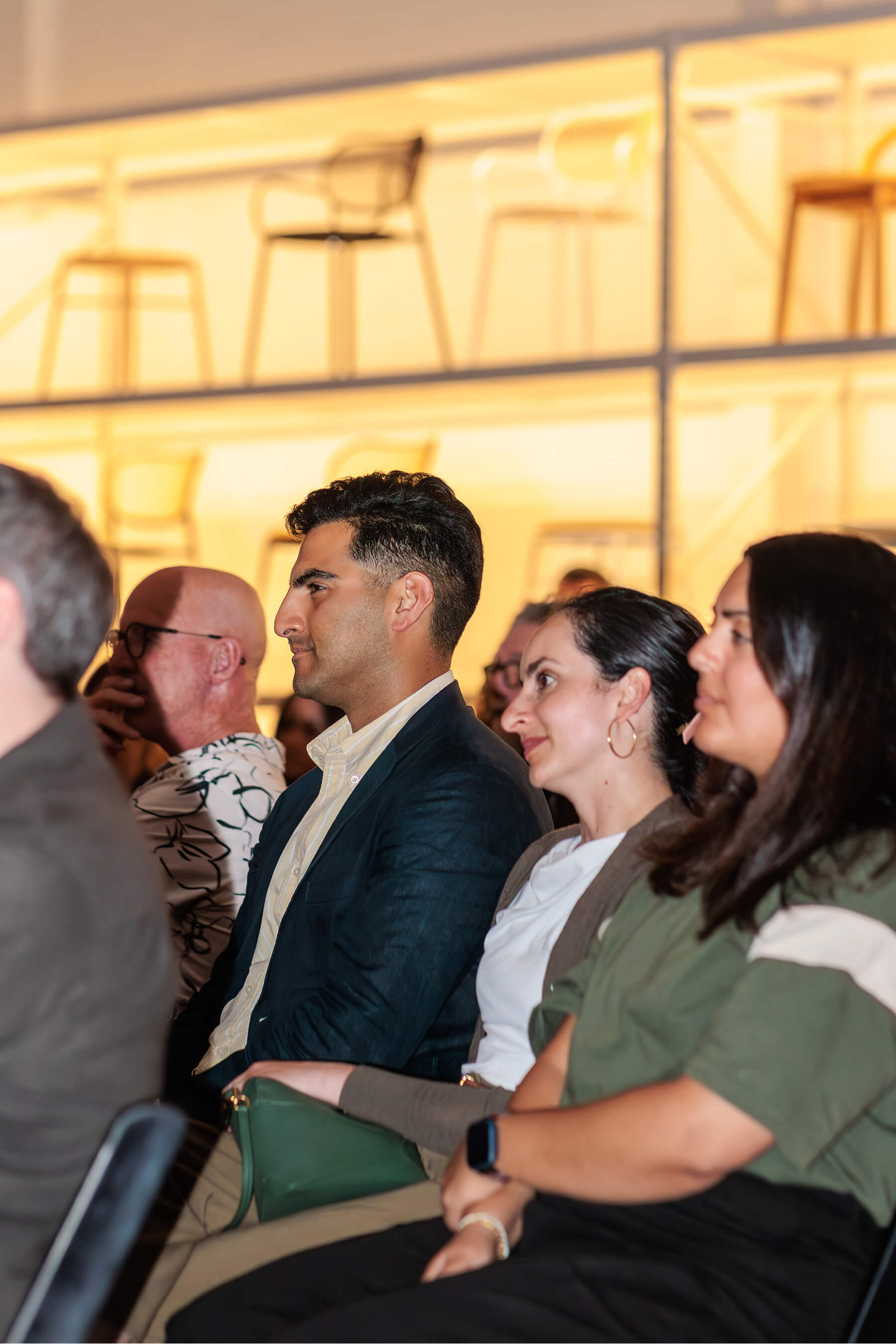 Audience members attentively watching the panel discussion, with a backdrop of modern designer chairs on illuminated shelving.