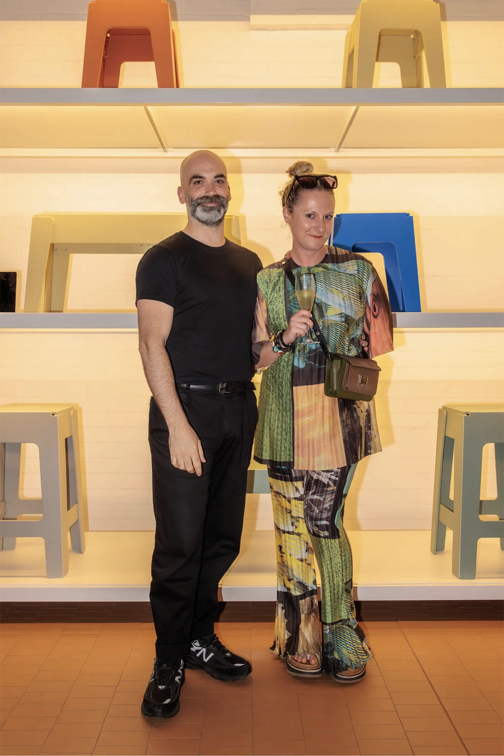 DesignByThem co-founder Nicholas Karlovasitis and a guest pose together in front of a shelving display featuring bright coloured DL stools.