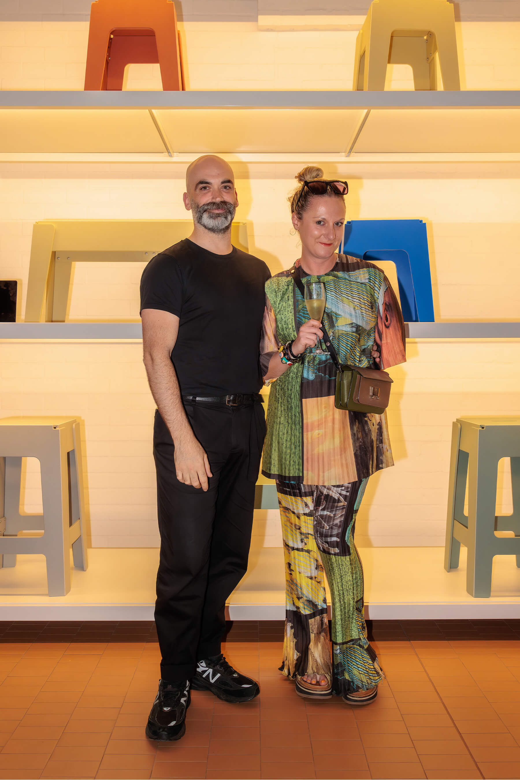 DesignByThem co-founder Nicholas Karlovasitis and a guest pose together in front of a shelving display featuring bright coloured DL stools.