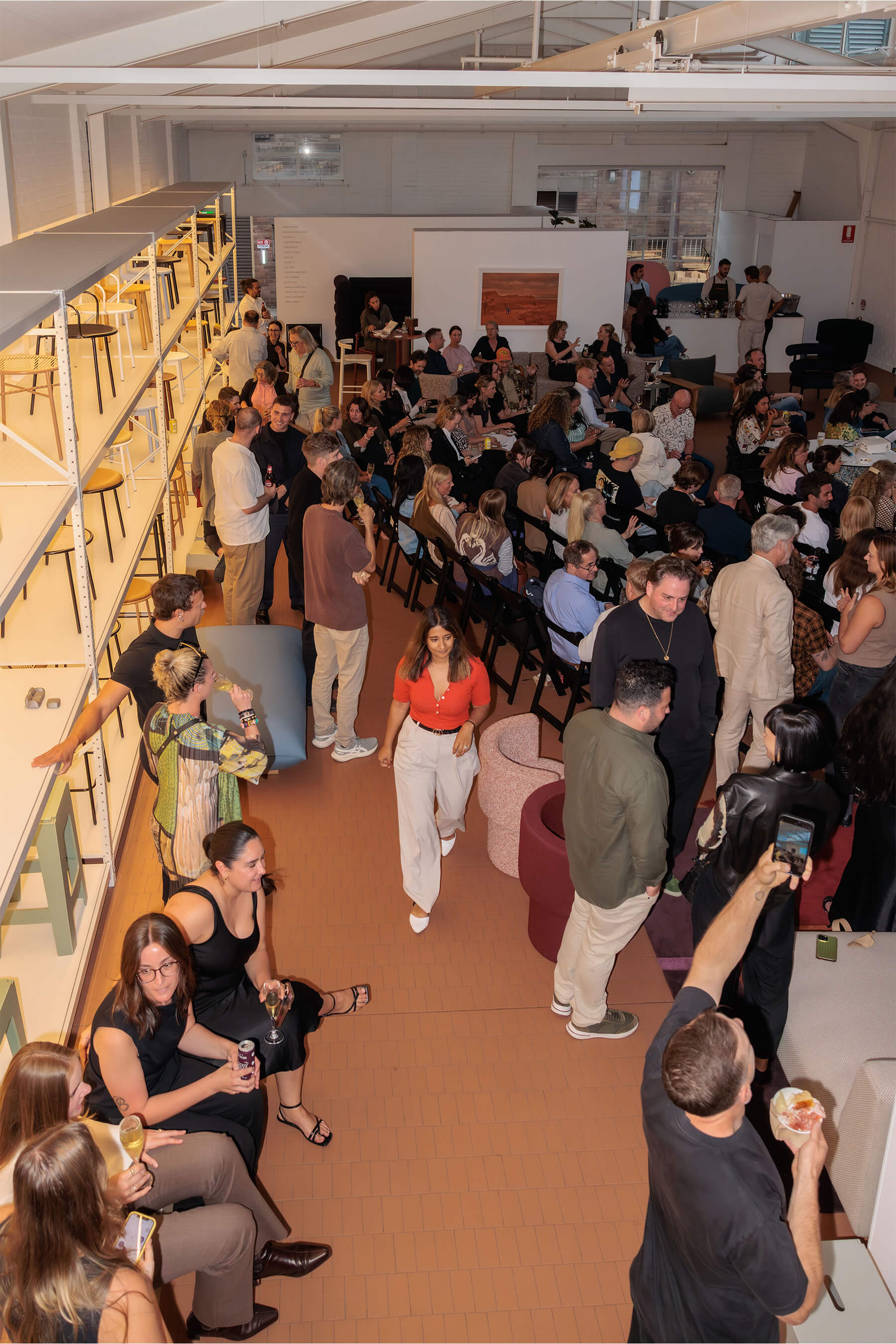 Overhead view of the full DesignByThem event audience, with guests mingling, chatting, and seated for the panel discussion.