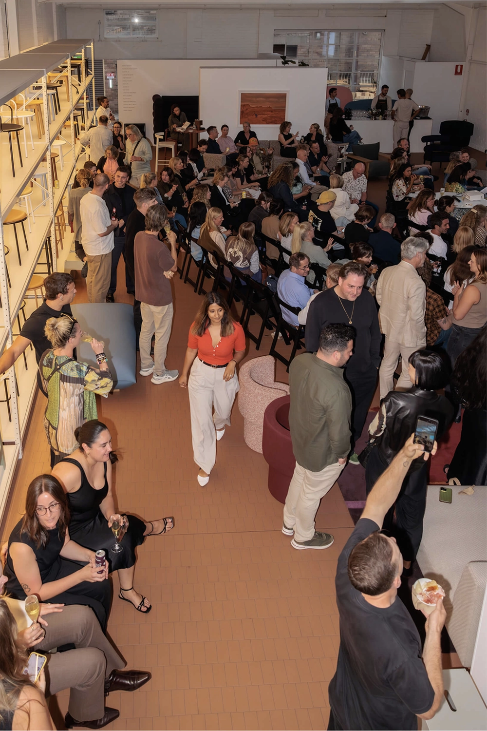 Overhead view of the full DesignByThem event audience, with guests mingling, chatting, and seated for the panel discussion.