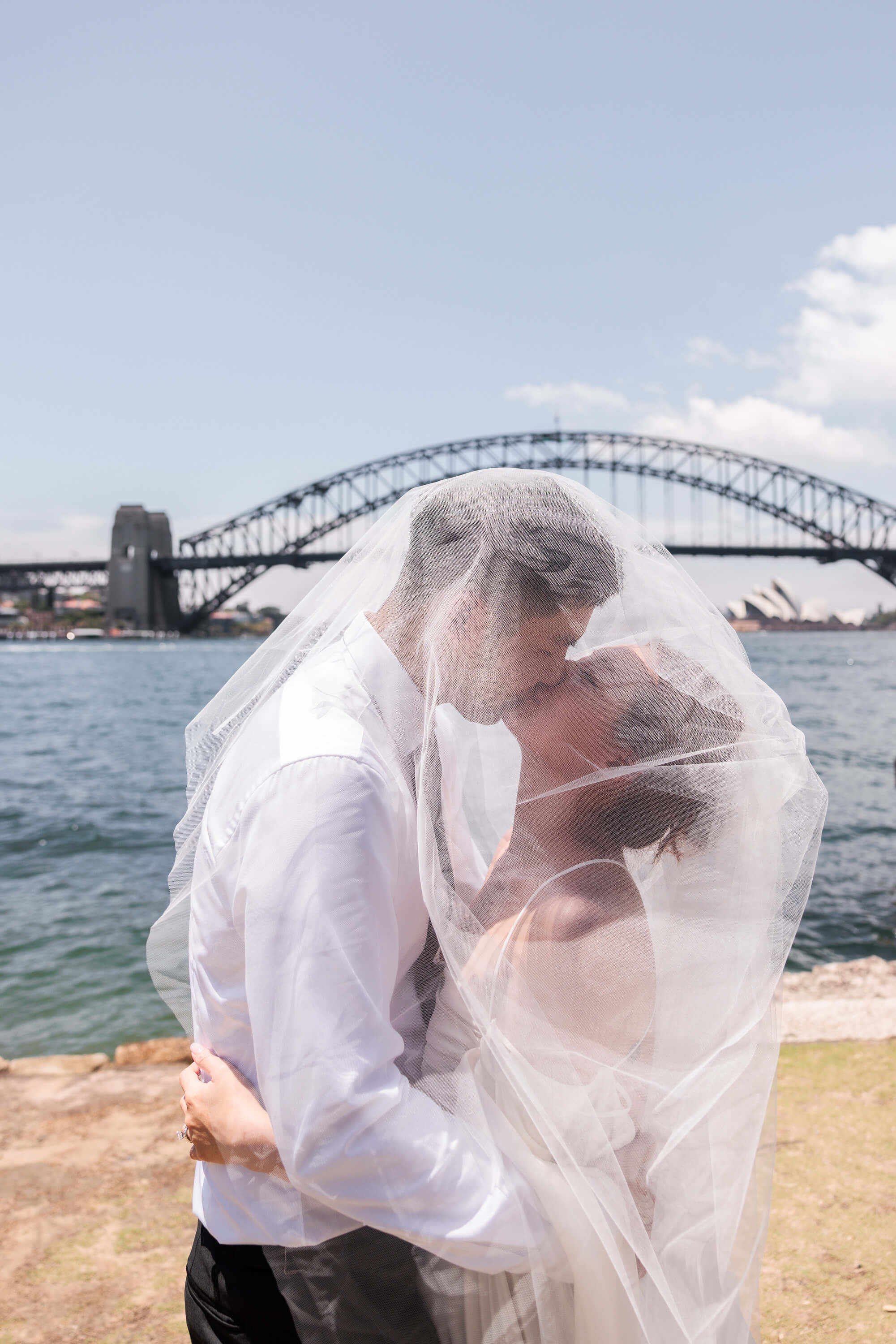 Melanie and Dai share a kiss beneath the veil by Sydney Harbour, marking the conclusion of their wedding portraits.