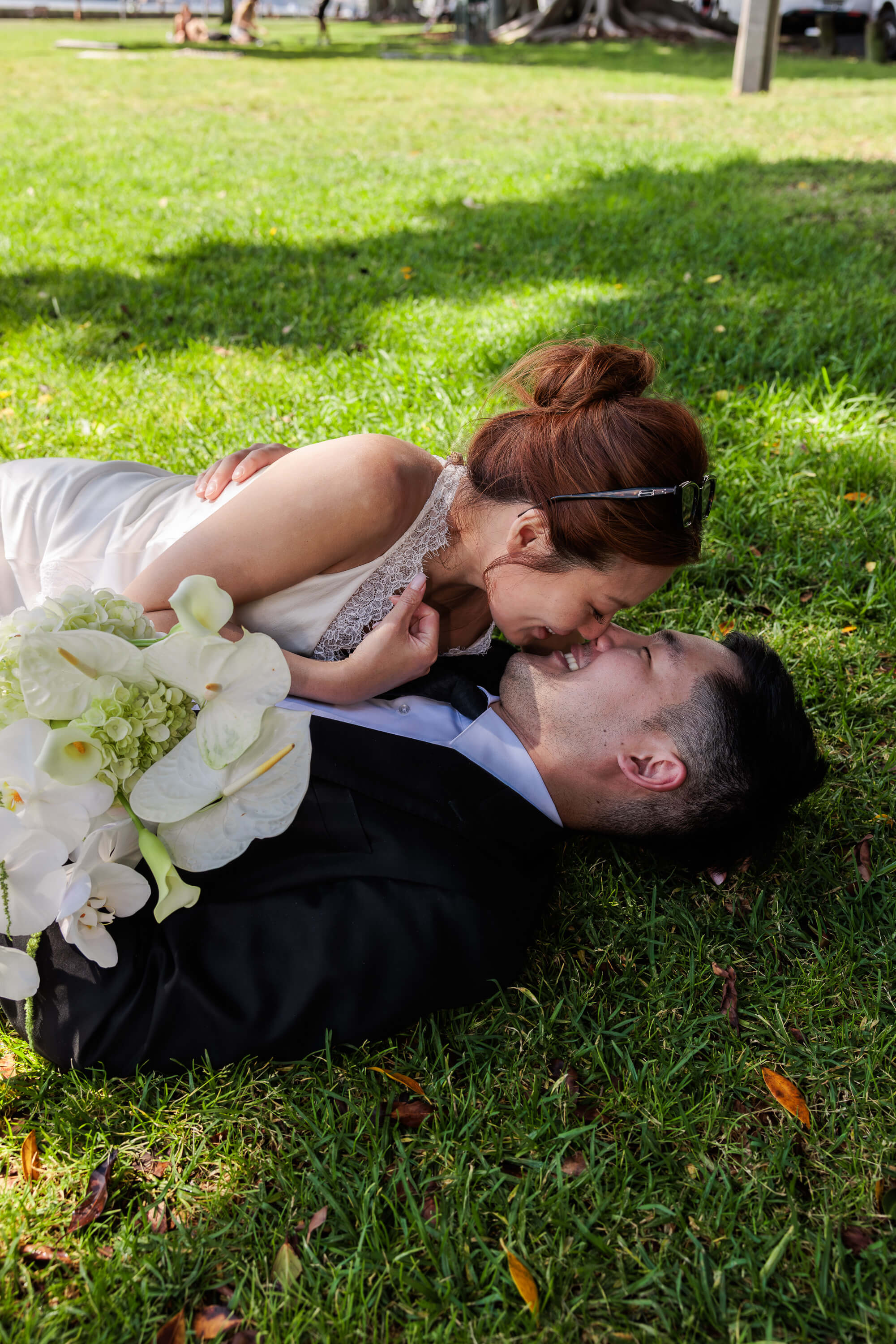 Melanie leans over Dai as they lie on the grass together, sharing an intimate and relaxed moment following their wedding.