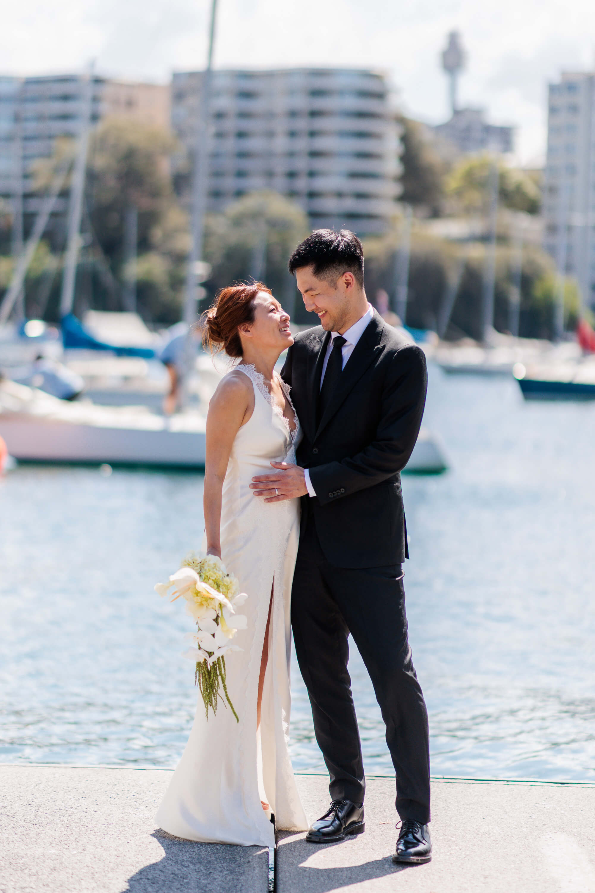Melanie and Dai smile at each other during a relaxed moment following their wedding ceremony by the harbour.