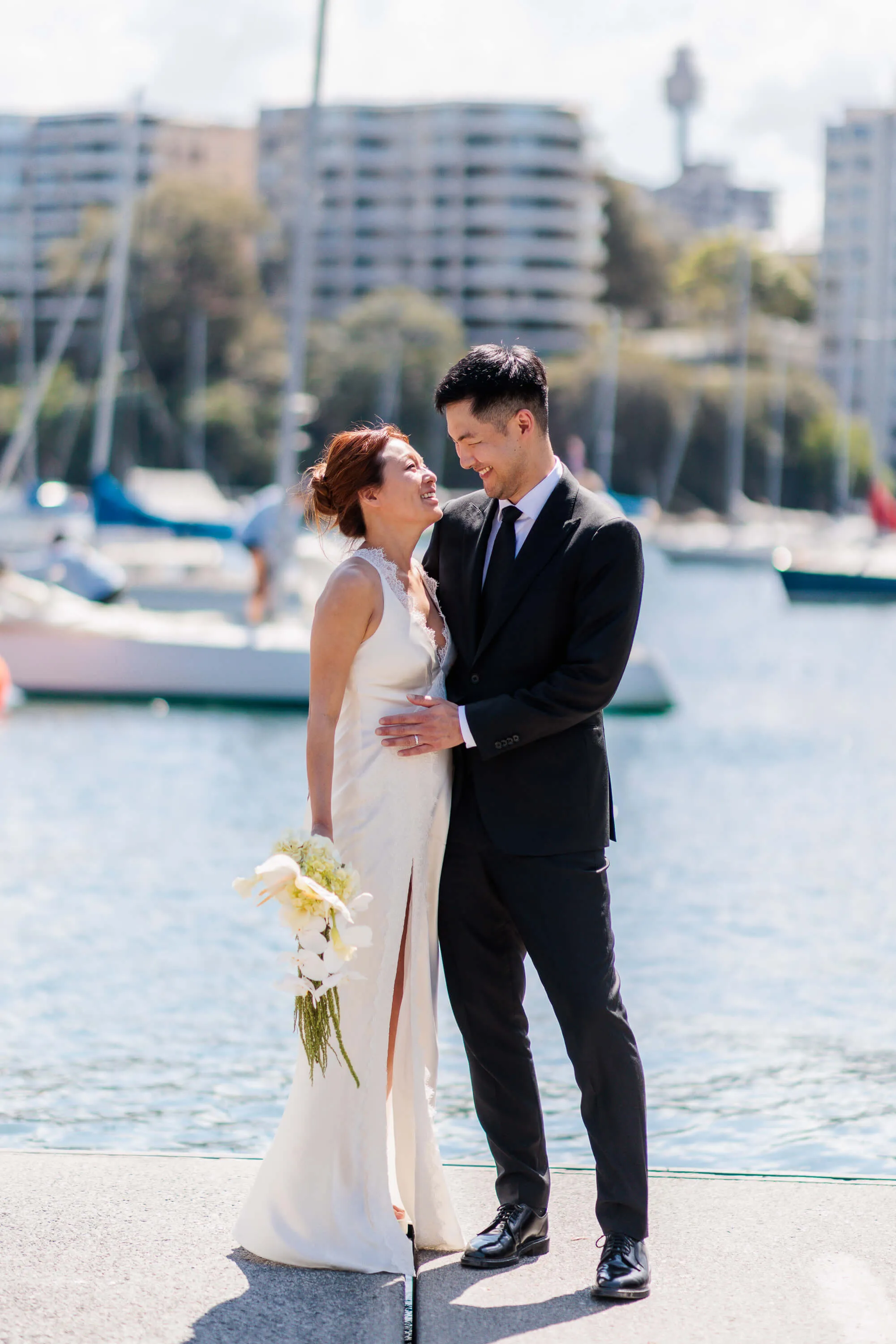 Melanie and Dai smile at each other during a relaxed moment following their wedding ceremony by the harbour | EDG Studios