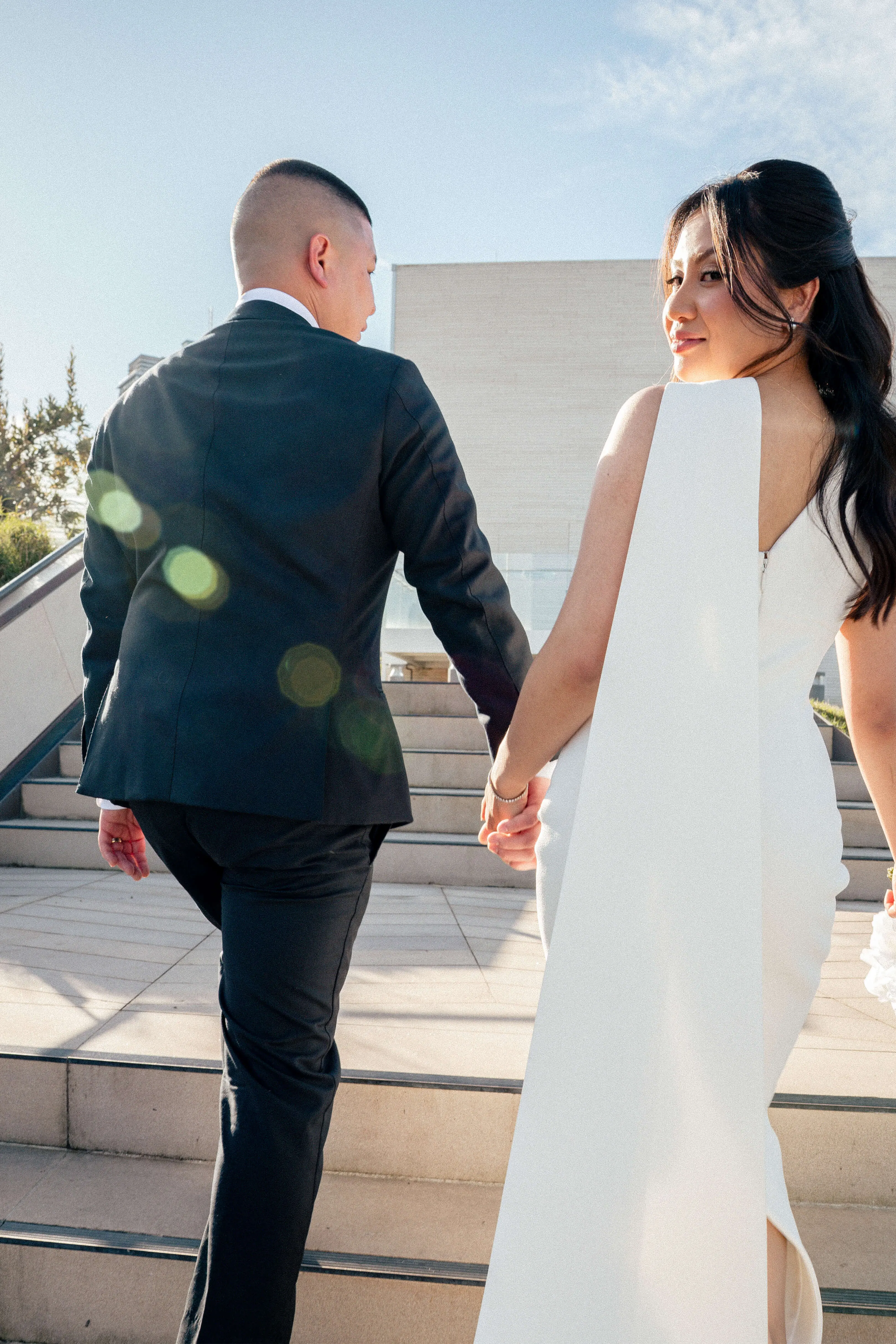 Walking up sandstone stairs post-ceremony, holding hands under a blue sky | EDG Studios