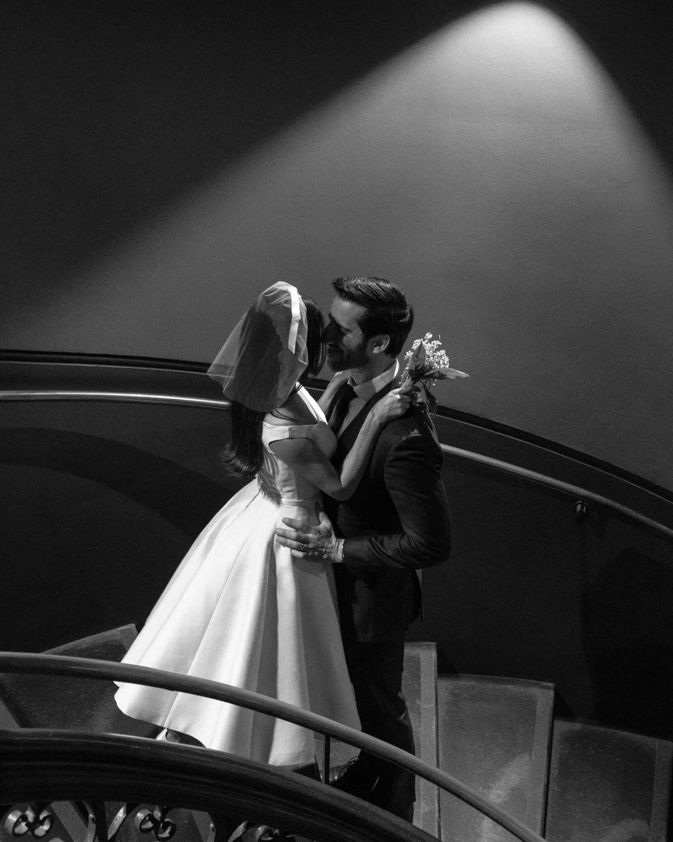 Mishti and Phil sharing a kiss on a curved staircase in Sydney