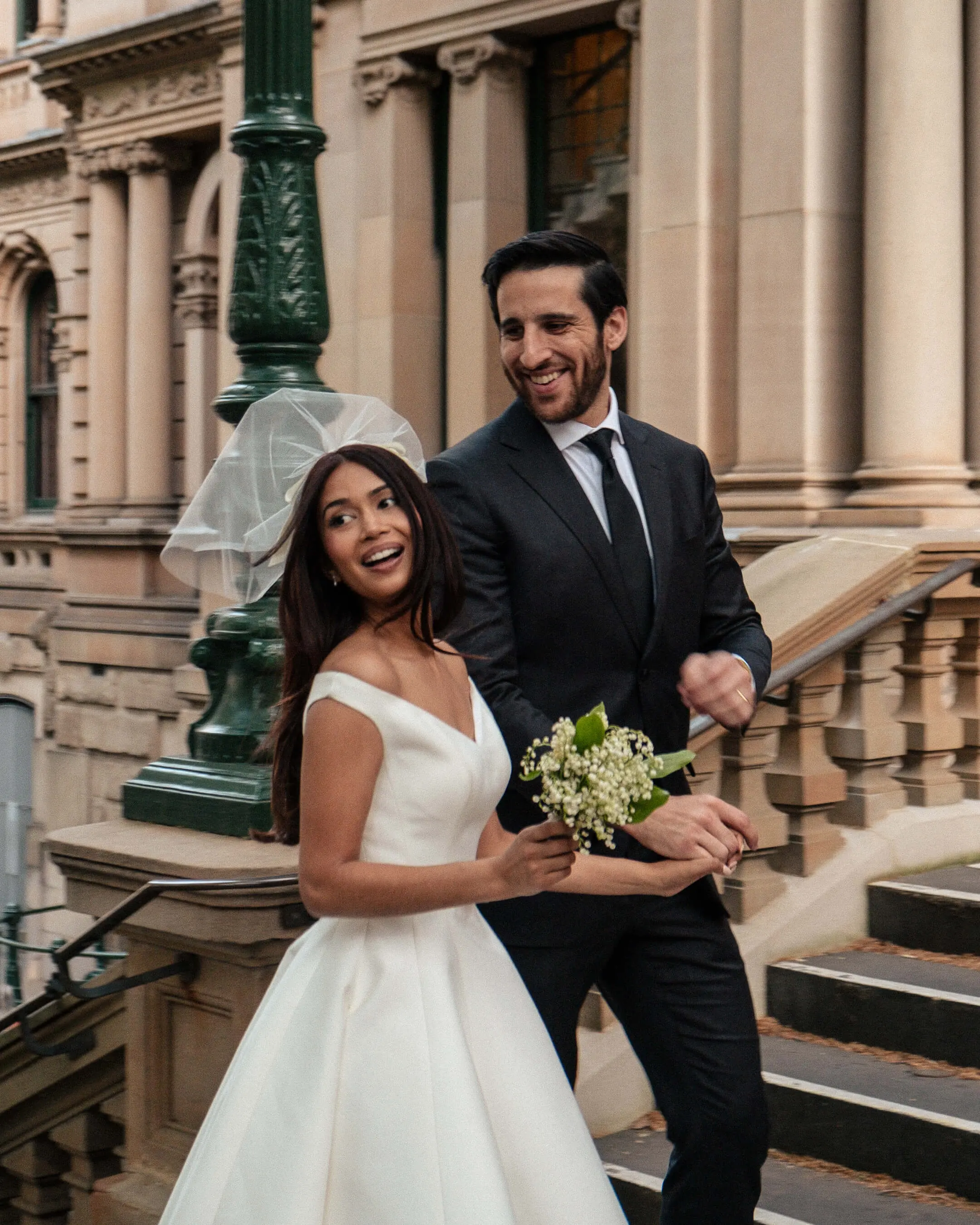 Mishti and Phil smiling together on sandstone steps during their wedding portraits.