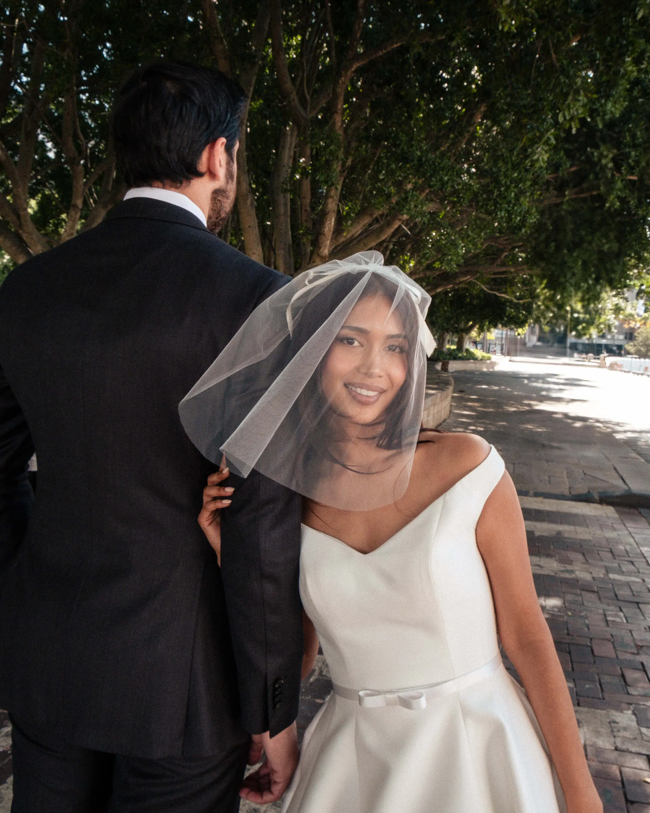 Mishti smiling beneath her veil beside Phil during their wedding portraits