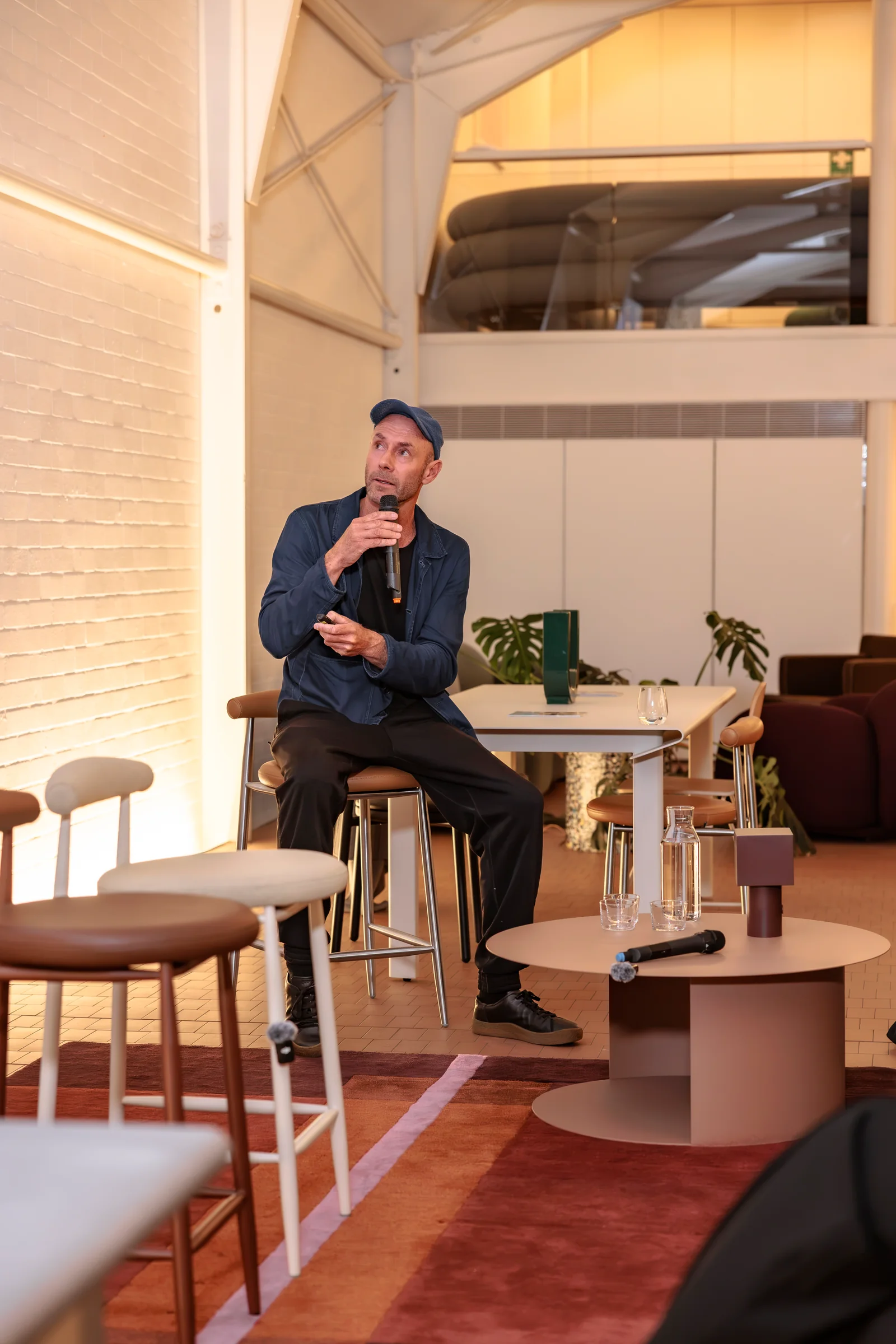 Speaker holding a microphone beside showroom furniture at Design By Them, photographed by EDG Studios.