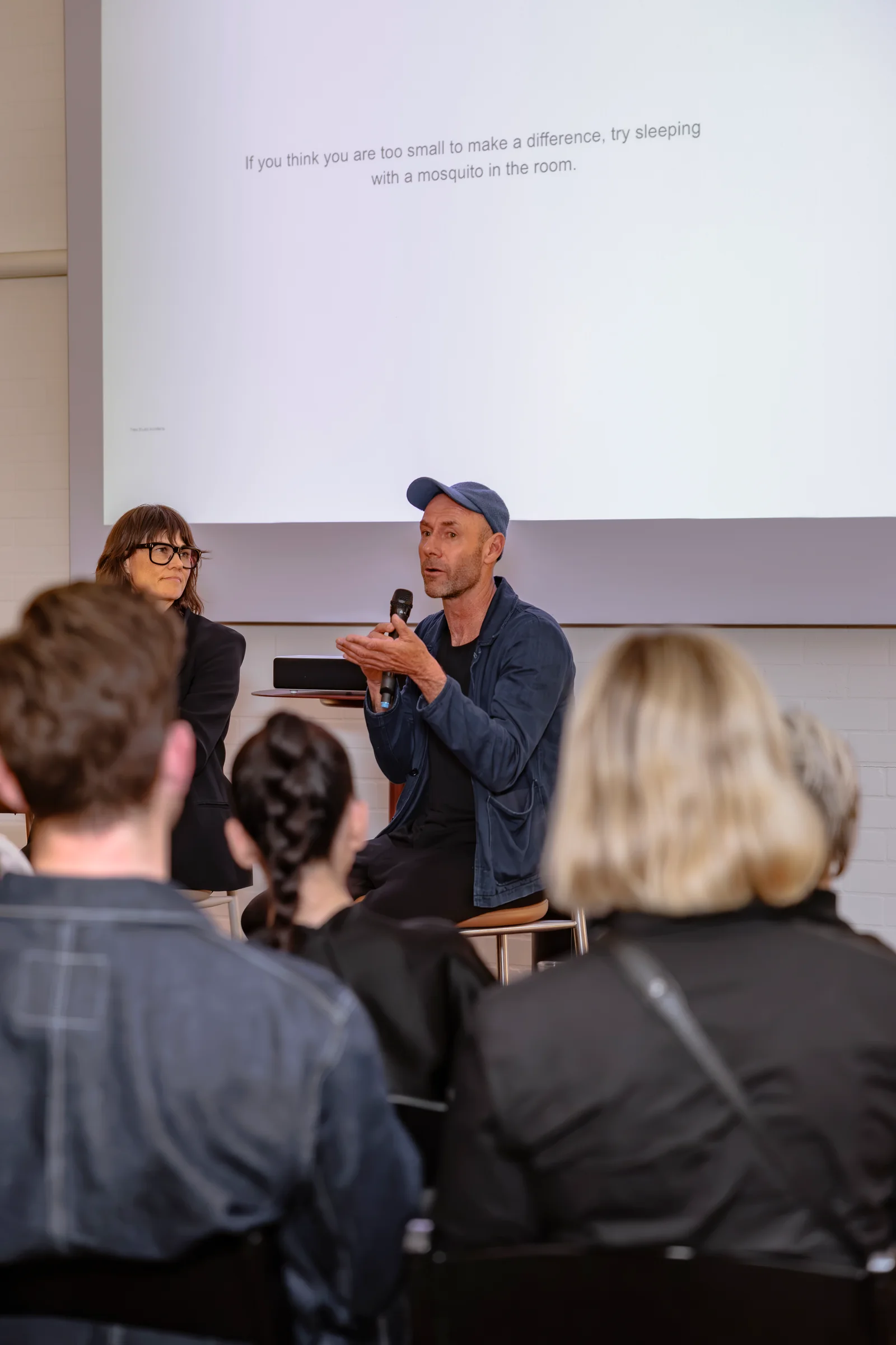 Speaker addressing the audience from a high stool at Design By Them, photographed by EDG Studios.