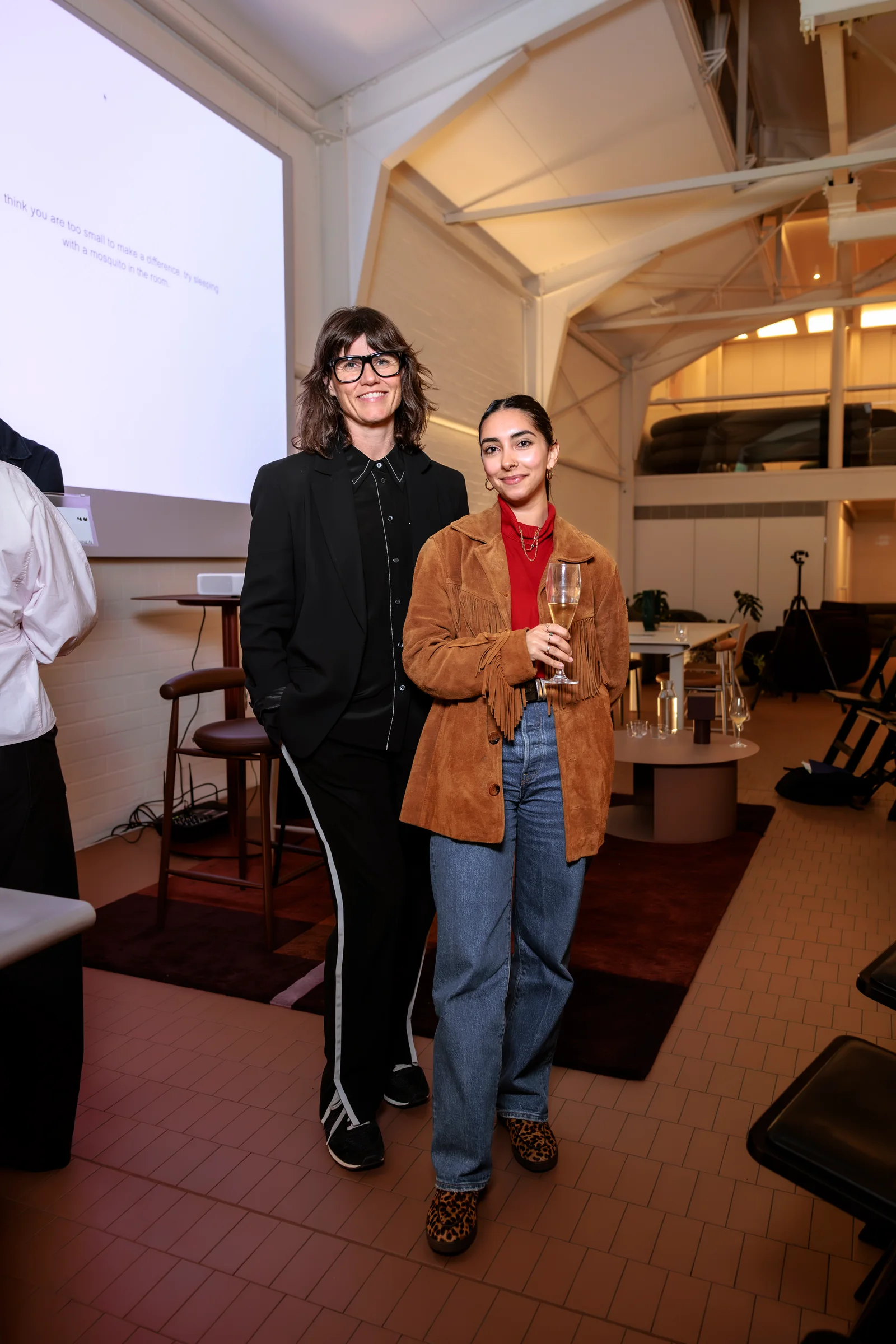 Two attendees smiling beside the presentation screen after the panel, photographed by EDG Studios.