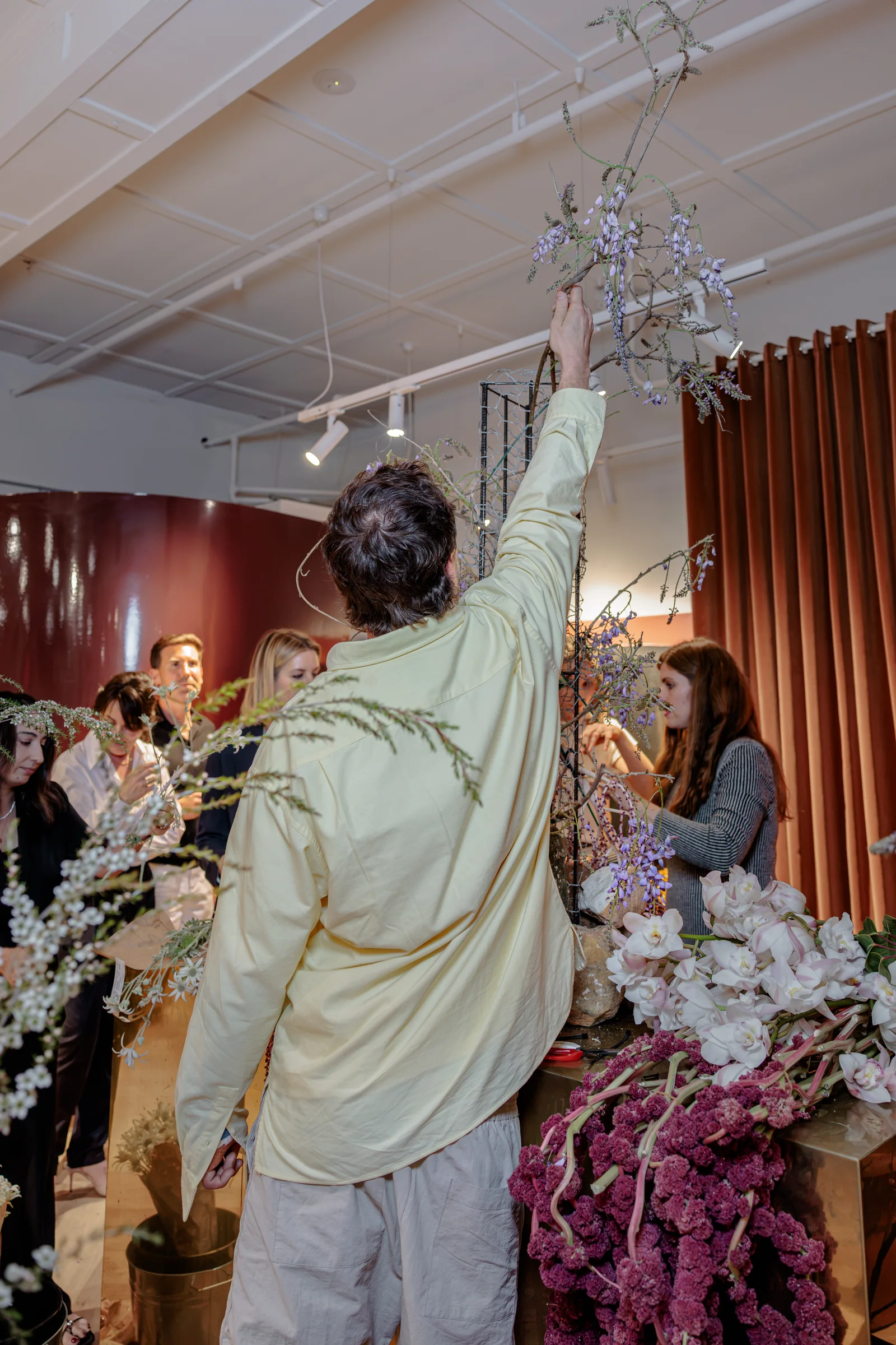 Florist reaching up to add branches to the tall floral installation, photographed by EDG Studios.
