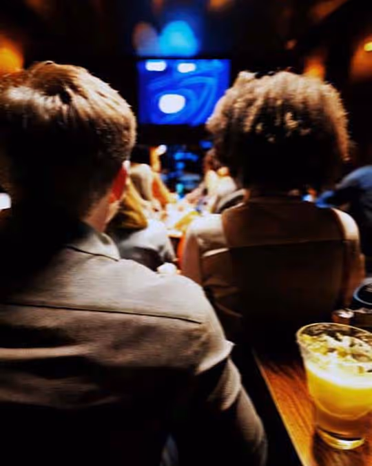 People gathered in a dark space, enjoying a movie together on a large screen, with their faces illuminated by the light.