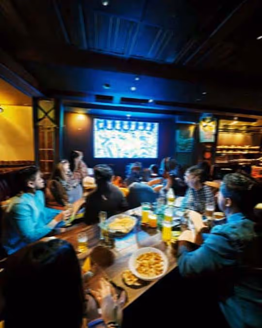 Several people gathered at a table, intently watching a movie on a screen, with popcorn and drinks in front of them.