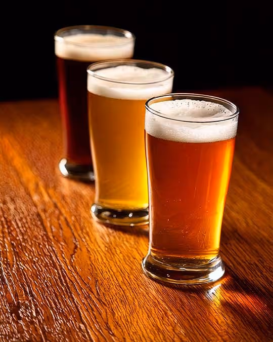 Three types of beer in glasses are arranged on a wooden table, each with a unique color and style, ready to be enjoyed.