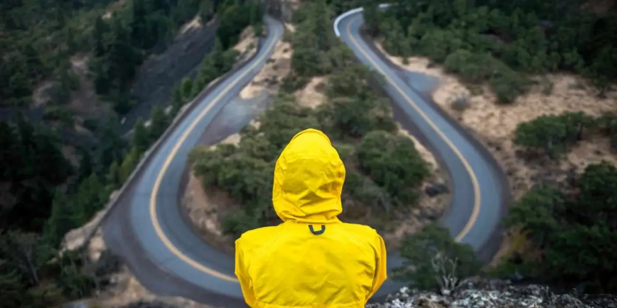 Yellow hooded figure looks down a winding road.
