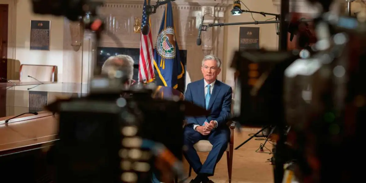 Jerome Powell sits in a studio with a US flag and microphone.