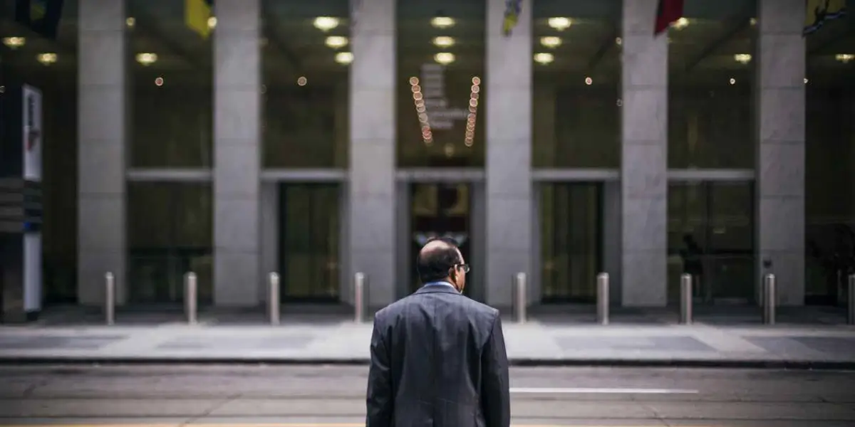 A man in a suit stands facing a building entrance.