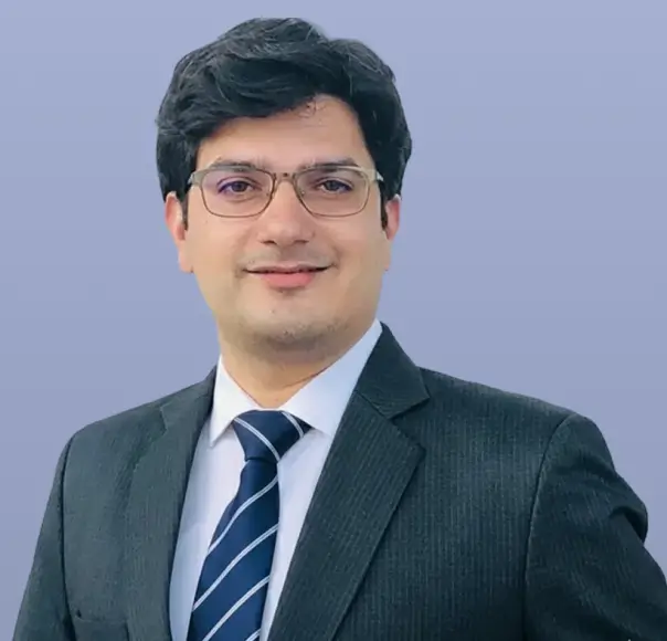 Manas Chadha, a man in a dark suit and tie, smiles neutrally.