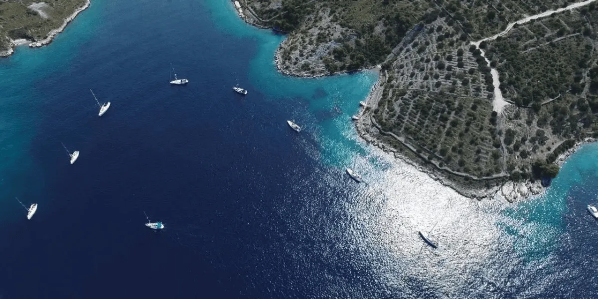 Blue water and sailboats in a rocky cove.