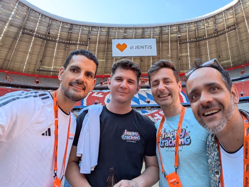 Four men smiling and posing for a selfie inside a large stadium with a 'JENTIS' sign in the background.