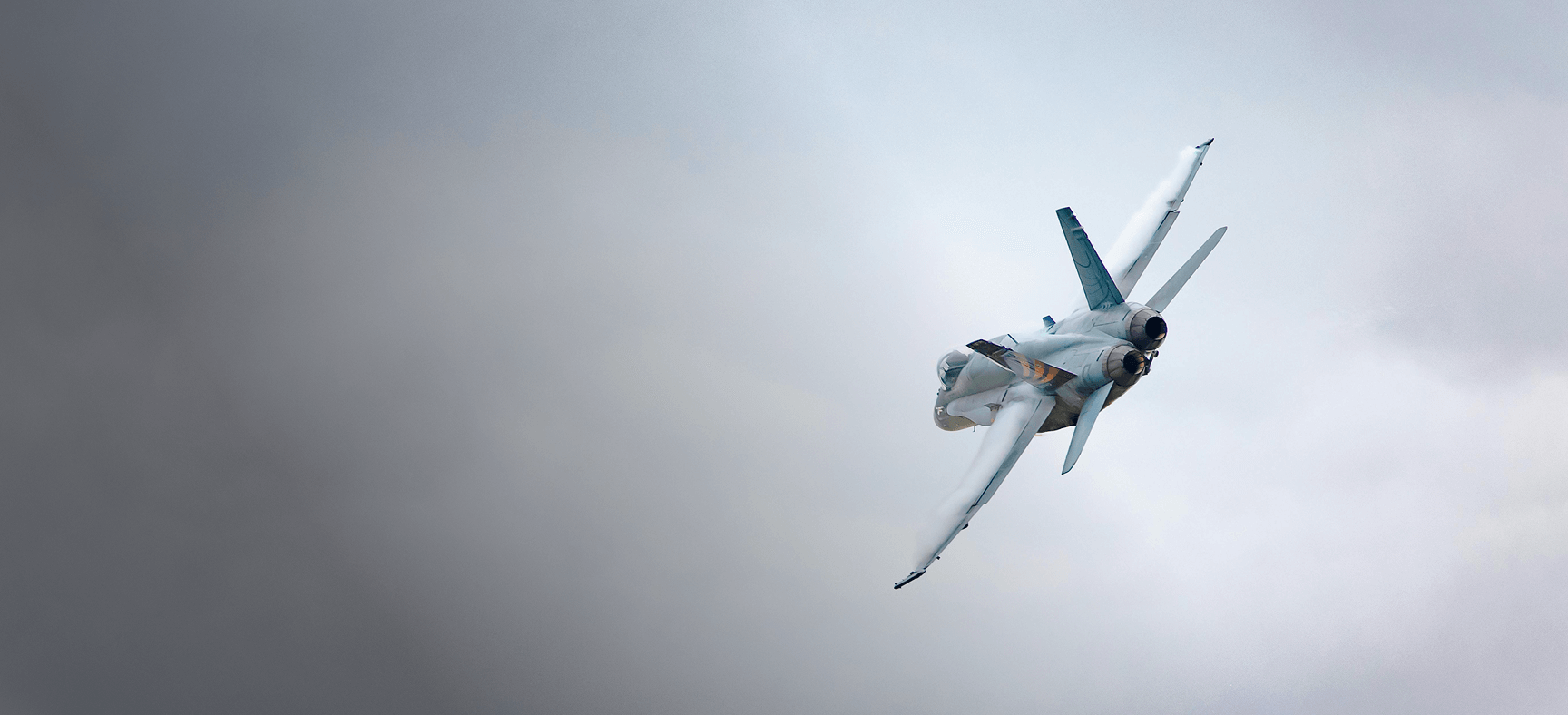 Jet fighter making a sharp turn in cloudy sky with vapor trails along its wings.