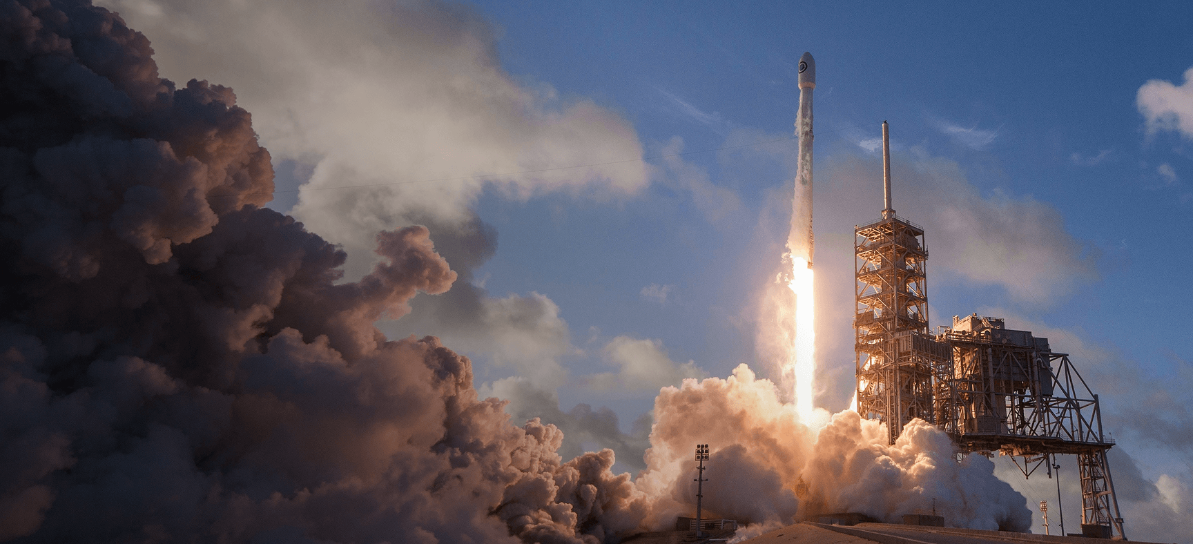 Rocket launching from a launchpad with large plumes of smoke and flames against a blue sky.