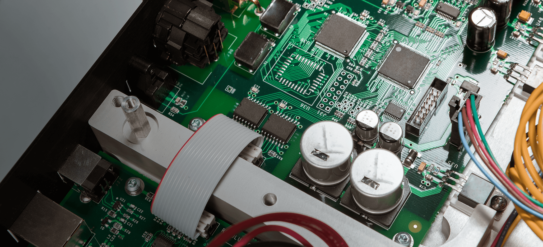 Close-up of a green electronic circuit board with capacitors, chips, wires, and connectors.