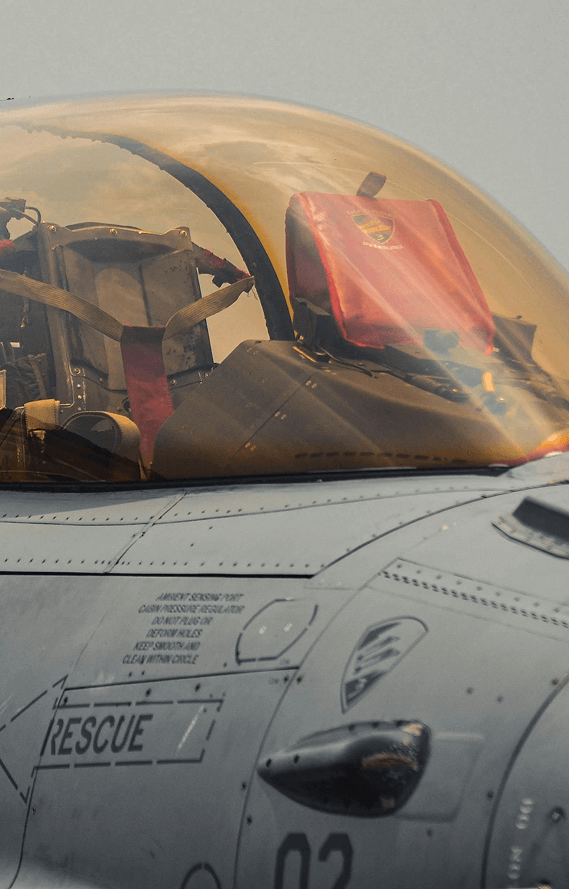 Close-up of a fighter jet cockpit with a red seat cover and clear canopy reflecting clouds.