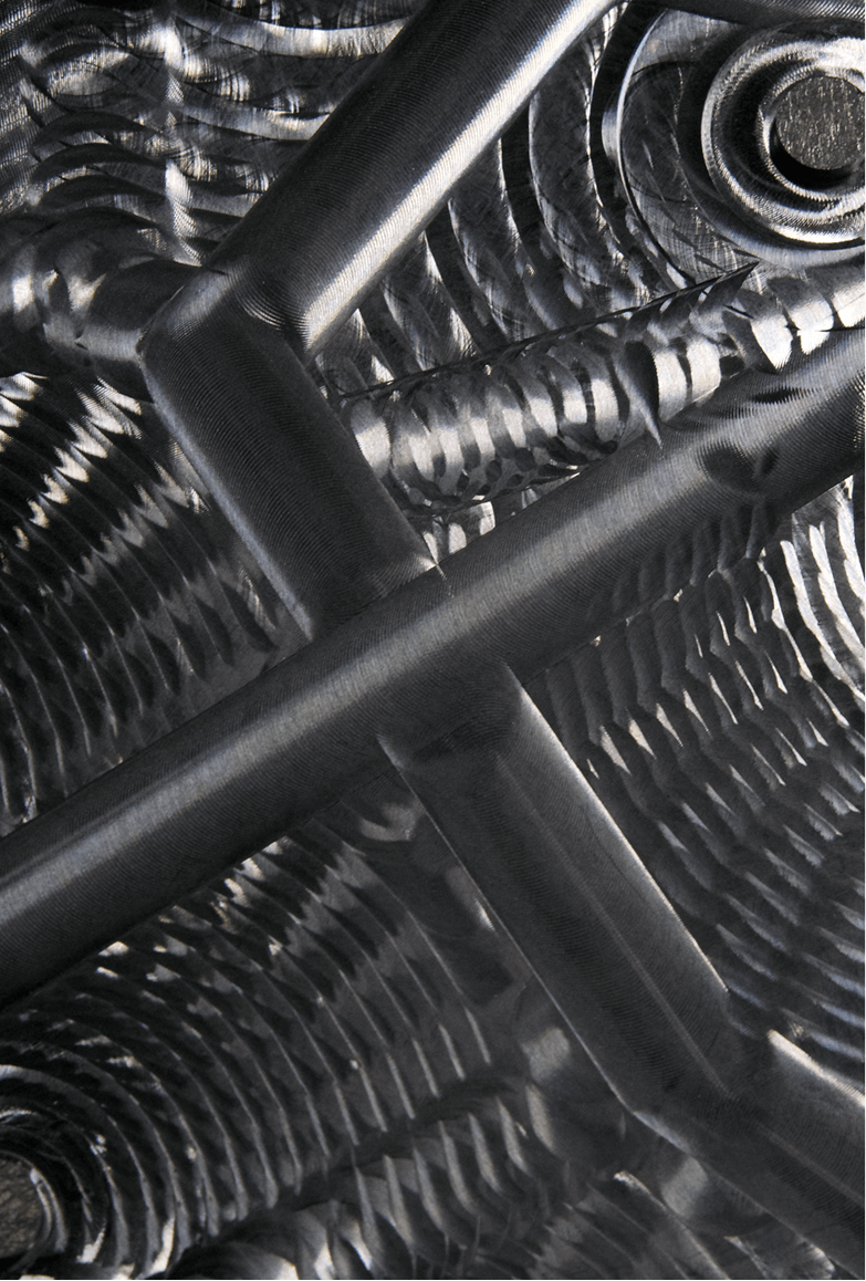 Close-up of intricate metallic structure with intersecting cylindrical rods and textured, patterned surfaces.