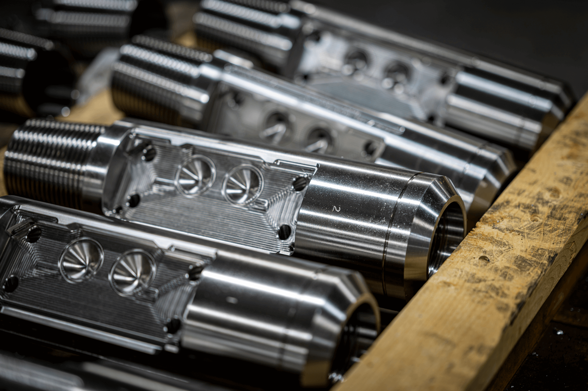 Close-up of several polished metal cylindrical components with threaded ends and grooves, arranged on a wooden surface.