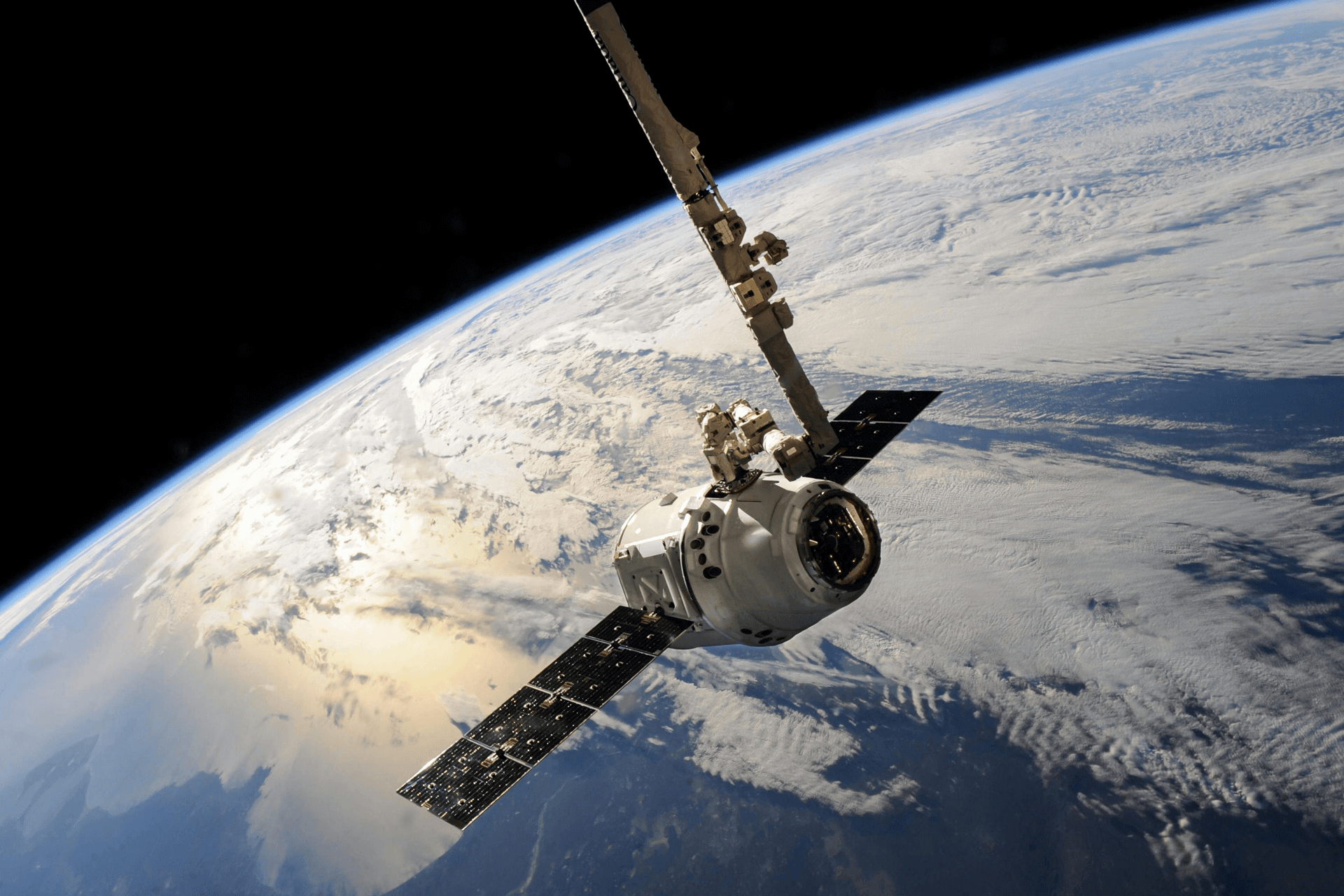 SpaceX Dragon spacecraft docked with robotic arm orbiting above Earth with cloud-covered planet surface below.