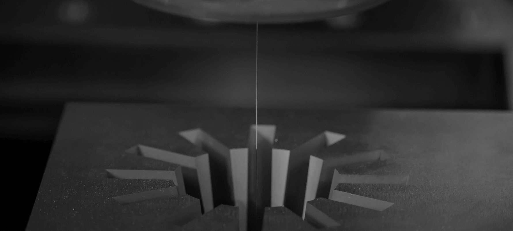 Close-up of a thin blade cutting a gear-shaped object with radial teeth in a dark setting.