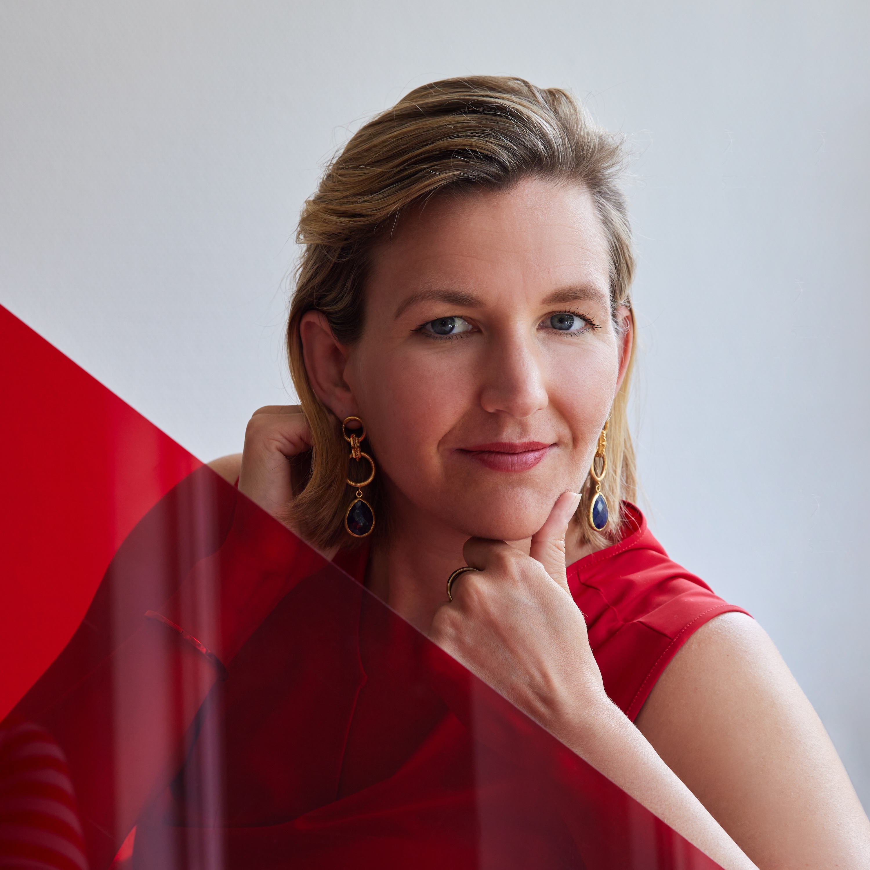 Simone hat blond gefärbte Haare und ein rotes Kleid und wird zum Teil von einem roten Quadrat im Vordergrund verdeckt.