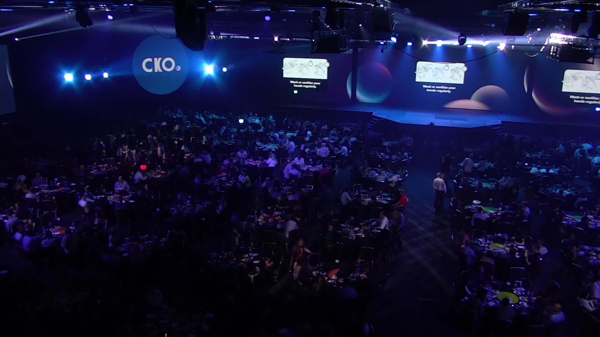 Wide view of the CKO room with LED screens around the stage
