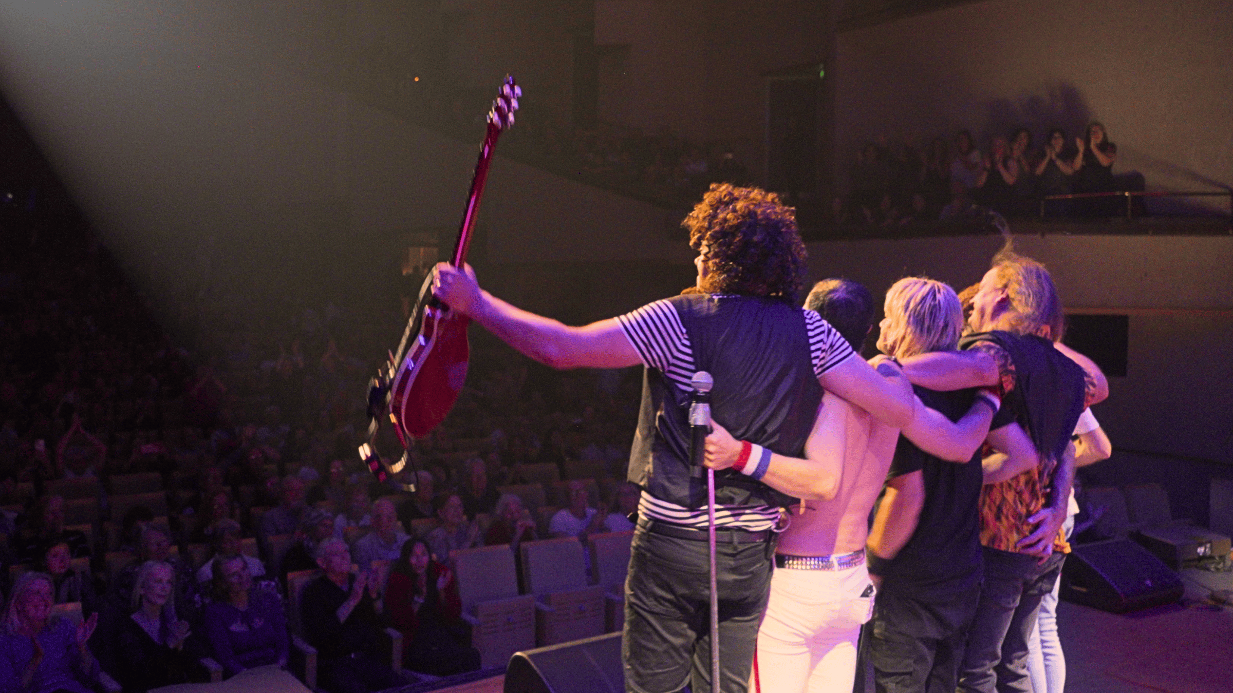 Queen Forever band members embracing on stage after the show