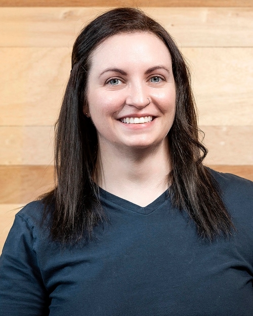 Headshot of a woman in a dark blue shirt against a wooden background.