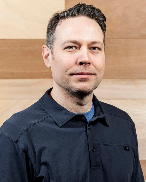 Headshot of man in dark blue button up shirt.